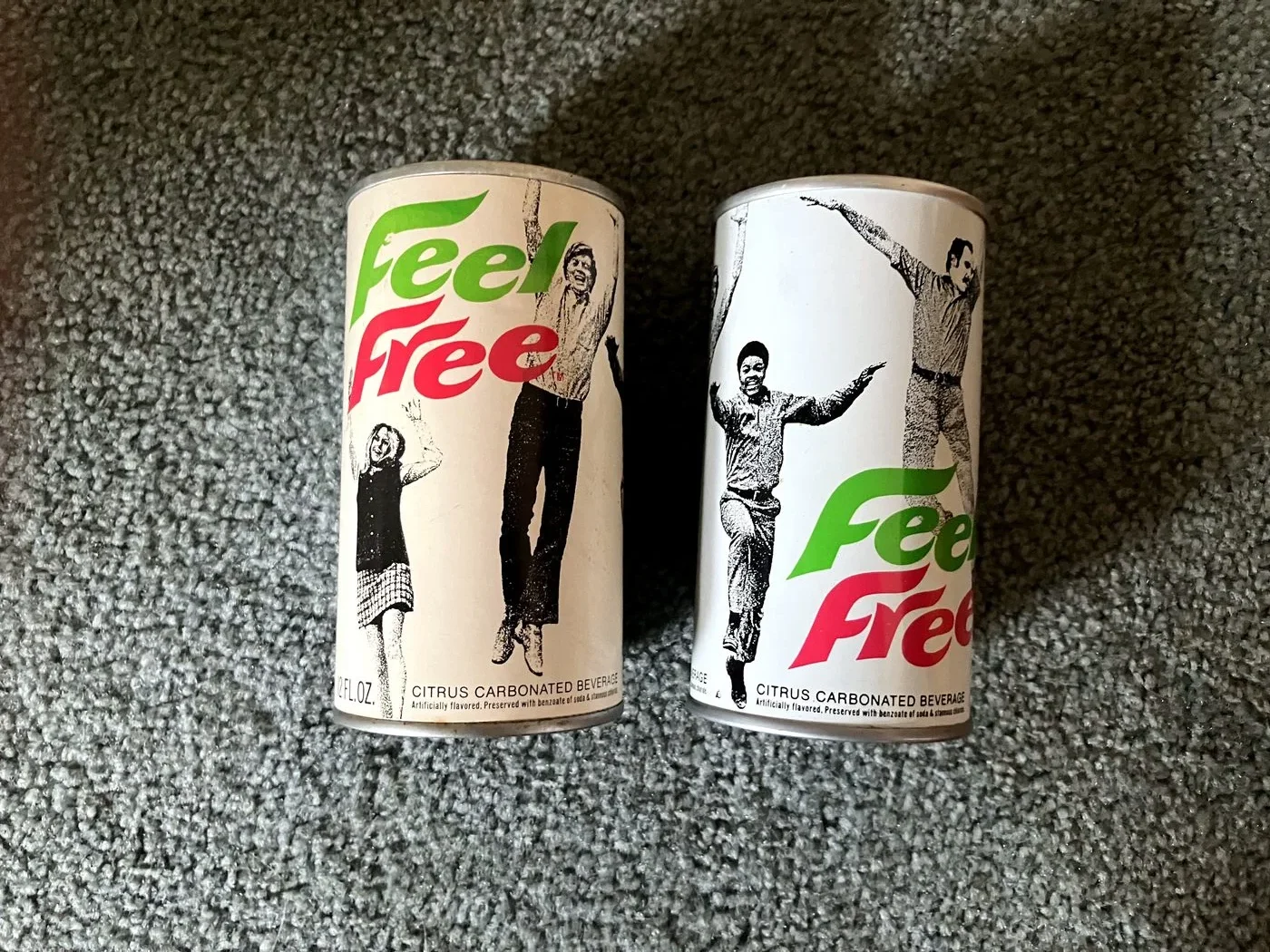 Two Feel Free citrus soda cans, white with red and green script lettering and black-and-white photographs of people jumping in the air.
